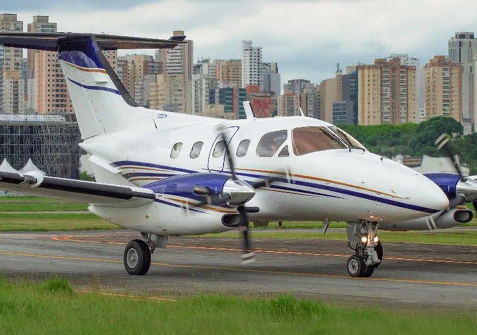 Avião bimotor turboélice taxiando na pista, com prédios residenciais ao fundo