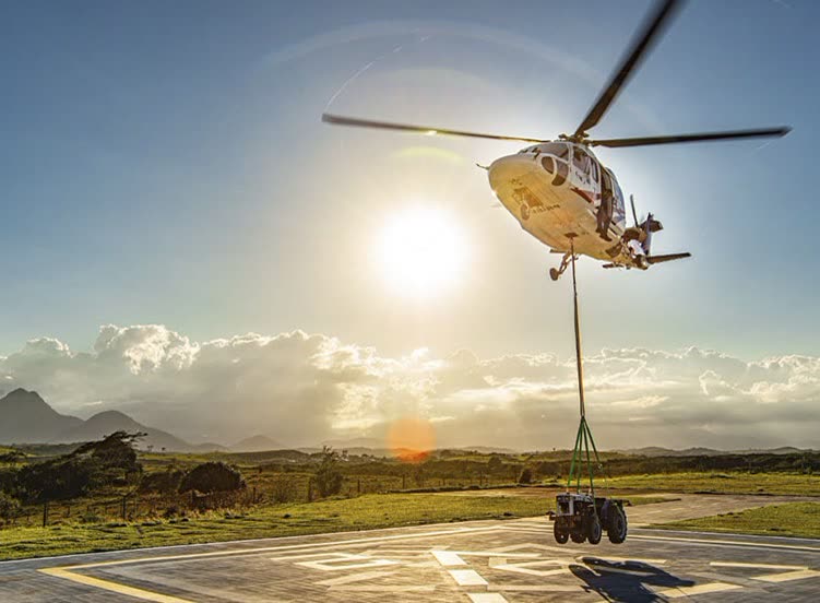 Contraluz de helicóptero erguendo um trator do heliponto com eslinga verde