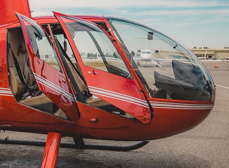 Cabine de helicóptero vermelho com as portas abertas e bancos de couro, no pátio do aeroporto