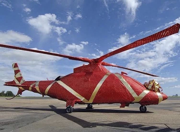 Helicóptero embrulhado em papel de presente vermelho com fitas e laço dourados, pousado no pátio