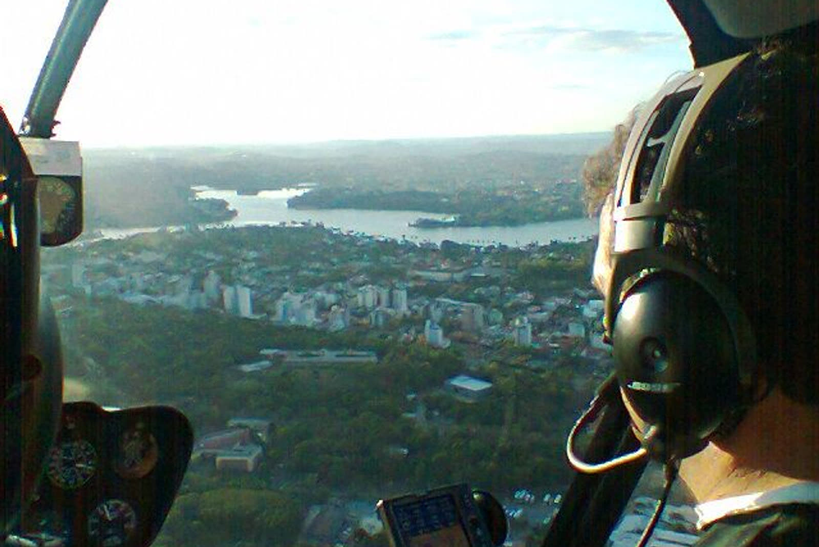 Vista da cabine do helicóptero: passageiro de fone observa a cidade, a mata e a represa
