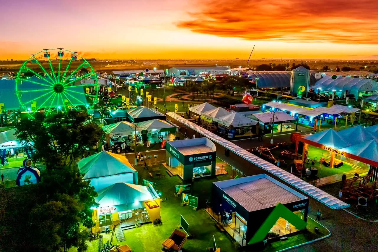 Feira agropecuária ao entardecer vista do alto, com roda-gigante, estandes e tendas iluminadas