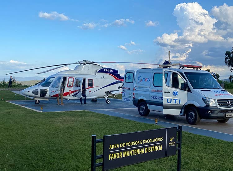 Helicóptero bimotor e ambulância UTI lado a lado em heliponto com placa de área de pouso